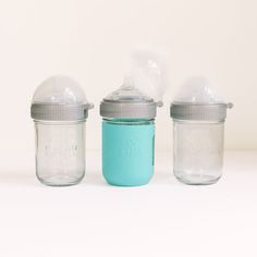 three glass jars with lids are lined up against a white background, one is empty and the other has a blue lid