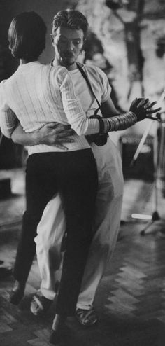 a man and woman dance together in an old black and white photo, with one holding the other's back