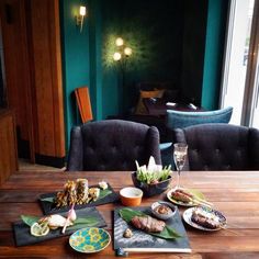 a wooden table topped with plates of food next to a glass of wine and two chairs