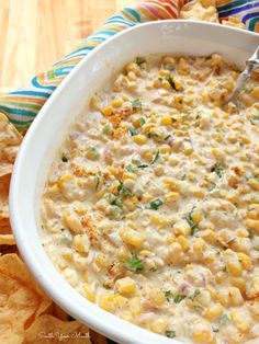 a white bowl filled with corn dip surrounded by tortilla chips