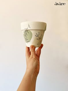 a hand is holding up a cup with designs on the outside and inside, in front of a white wall