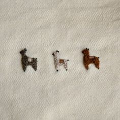 three small embroidered llamas sitting on top of a piece of white linen fabric