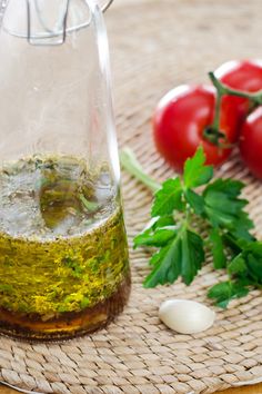 a glass bottle filled with olive oil next to tomatoes and parsley