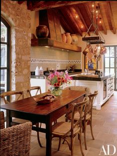 a dining room table and chairs in front of an open kitchen with wooden ceiling beams