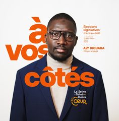 a man wearing glasses standing in front of an orange and white poster with words on it