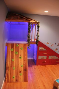 a room with a climbing wall and wooden flooring in the corner, under a purple light