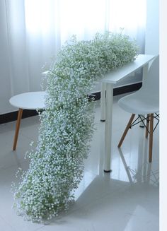 a white table topped with lots of baby's breath next to a chair and window