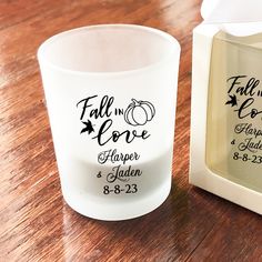 a glass with the words fall in love on it next to an empty candle holder