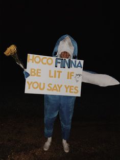 a man dressed as a shark holding a sign that says hoco finna be lit if you say yes