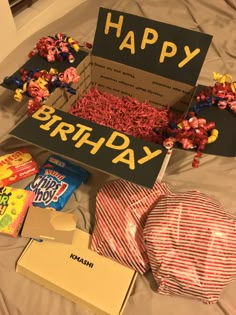 a birthday box filled with candy and candies on top of a bed next to a sign that says happy birthday