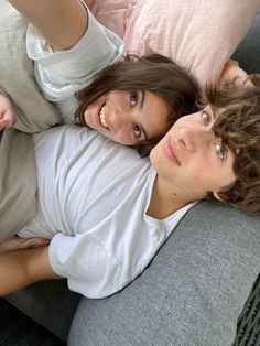 two people laying on a couch with their arms around each other and looking at the camera