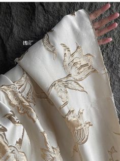 a person's hand is holding onto a white and gold floral print fabric with flowers on it