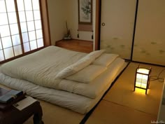 a bed with white sheets and pillows on top of it next to a lamp in front of a window