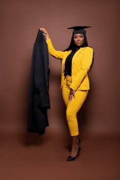 a woman in a yellow suit and black graduation cap holding up a black jacket on a brown background