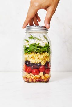 a hand reaching into a mason jar filled with pasta, beans, and spinach