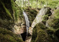 a small waterfall in the middle of some mossy rocks and trees on either side