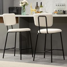 two white bar stools in front of a counter with wine glasses and bottles on it