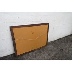 a brown framed painting sitting on the side of a white wall next to a cement floor