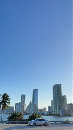 two cars are parked in front of the water and city buildings on a sunny day