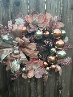 a wreath with pink and gold ornaments on it hanging on a wooden fence in front of a house