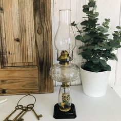 a glass lamp sitting on top of a white table next to a potted plant