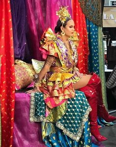 a woman sitting on top of a bed covered in colorful fabrics