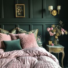 a bed covered in pink and green pillows next to a table with flowers on it