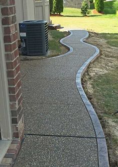 a paved walkway in front of a house with an air conditioner on the side