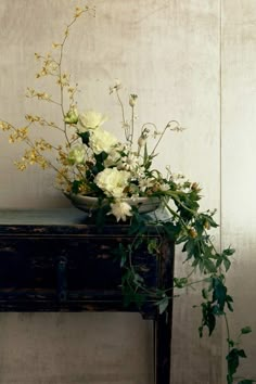 a vase filled with white flowers sitting on top of a wooden table next to a wall