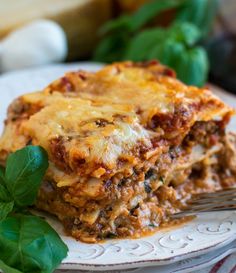 a white plate topped with lasagna covered in sauce and cheese next to green leaves