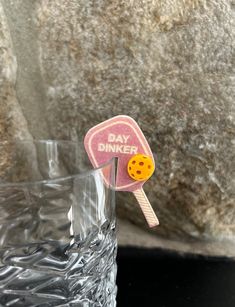 a pink and yellow pin sitting on top of a glass next to a stone wall