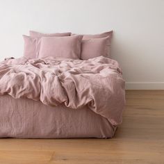 an unmade bed with pink linens and pillows on top of it in a white room