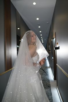 a woman in a white wedding dress is walking down the hallway with a veil on her head