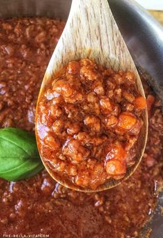 a wooden spoon filled with chili sauce and basil on top of a pot full of beans