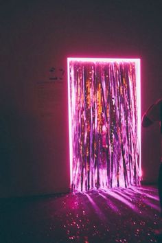 a person standing in front of a purple and pink wall with lights on the floor