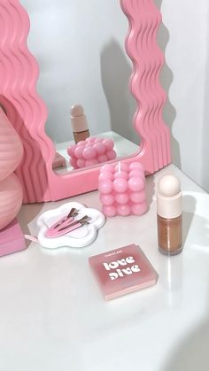 a vanity with pink accessories on it and a mirror in the back ground, next to a book