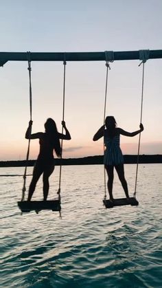 two girls on swings in the water at sunset