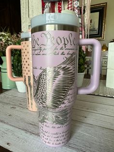 a pink and blue travel mug sitting on top of a wooden table