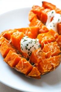 two sweet potatoes on a white plate with sour cream and chives in the middle