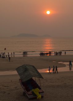 a boat on the beach at sunset with people in the background