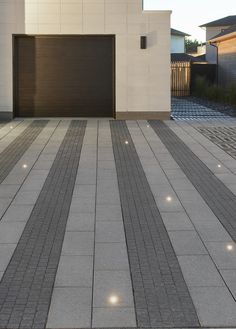 an empty driveway with two garage doors in the background and lights on either side of it