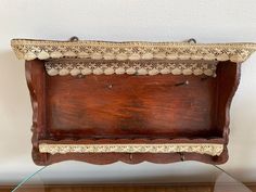 an old wooden box with lace trim on the top and bottom, sitting on a glass table