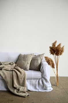 a white couch sitting on top of a floor next to a vase with dried flowers