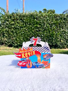 a toy car is sitting on top of a white table in front of some bushes