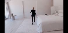 a woman in a black suit is walking into a white room with a large bed