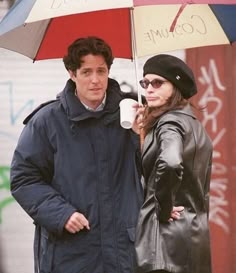 a man standing next to a woman under an umbrella on the street while holding a coffee cup