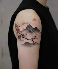 a woman's arm with a mountain and cherry blossom tattoo on her left shoulder