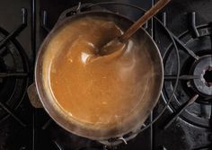 a pot filled with liquid sitting on top of an open burner oven door next to a wooden spoon