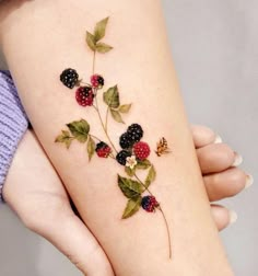 a woman's leg with berries and leaves on it, while she is wearing a tattoo