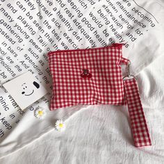 a red and white checkered bag sitting on top of a bed next to a tag